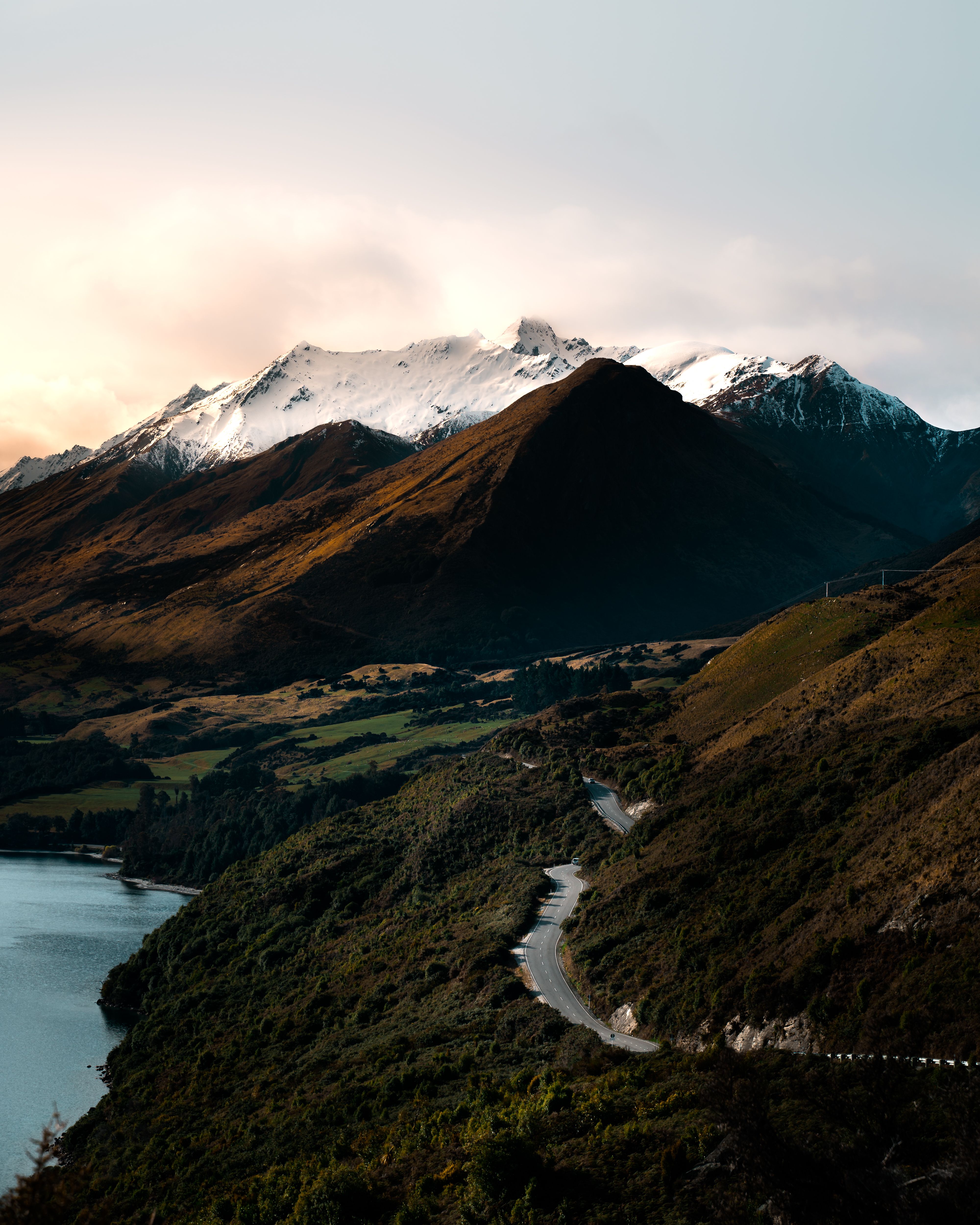 Scenic view of New Zealand's snow-capped mountains with a winding road at sunrise.