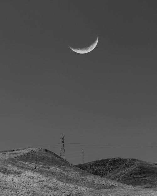 Monochrome Photo of a Transmission Tower Under a Crescent Moon