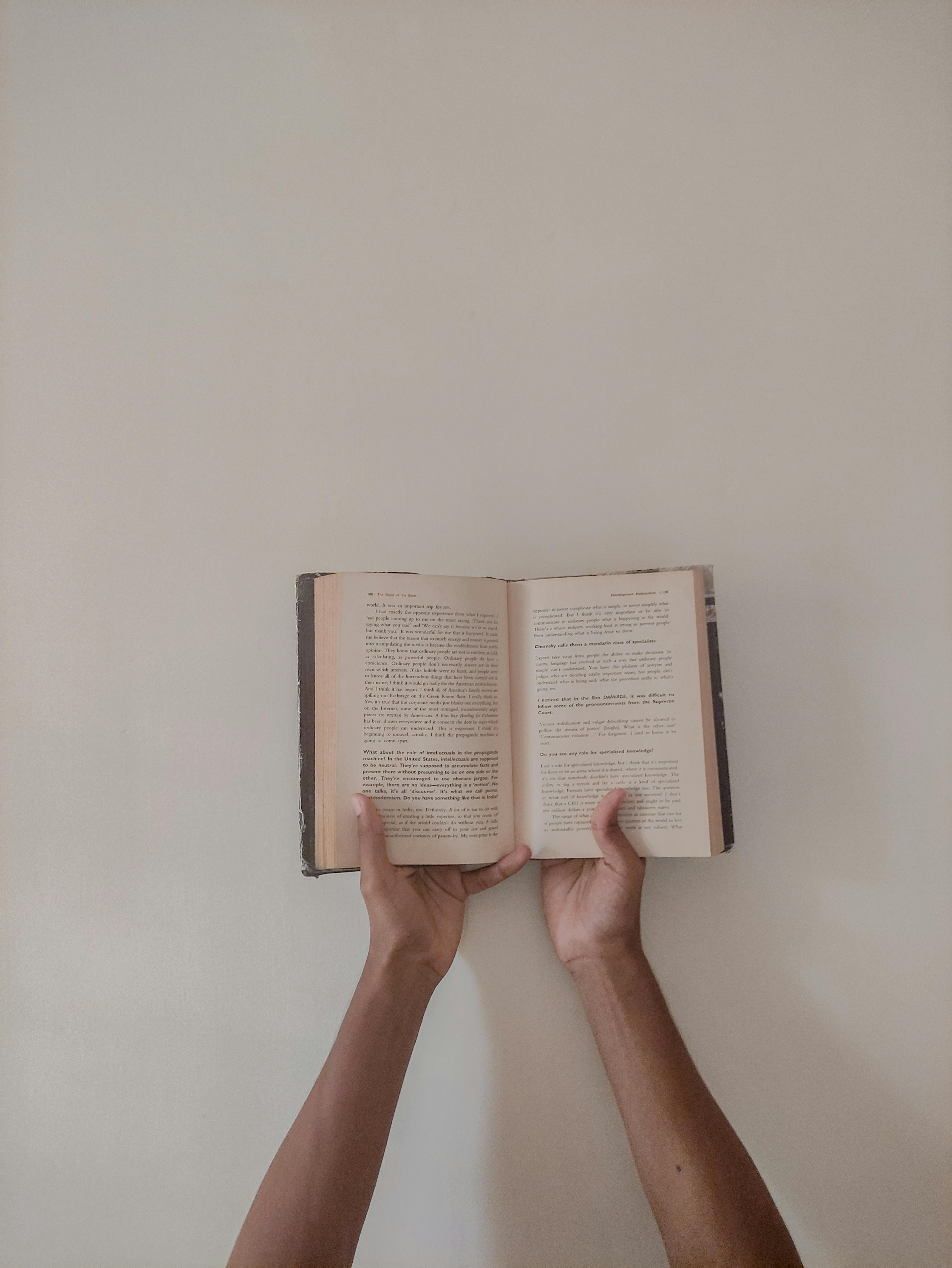 Minimalist photograph of hands holding an open book against a plain background, emphasizing simplicity and focus.