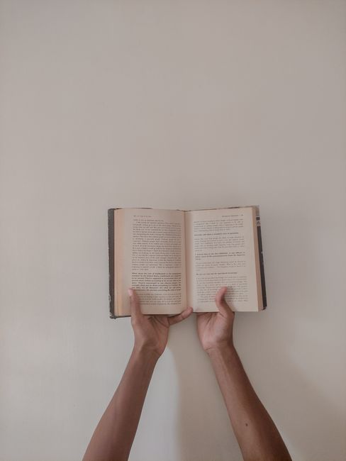 Minimalist photograph of hands holding an open book against a plain background, emphasizing simplicity and focus.