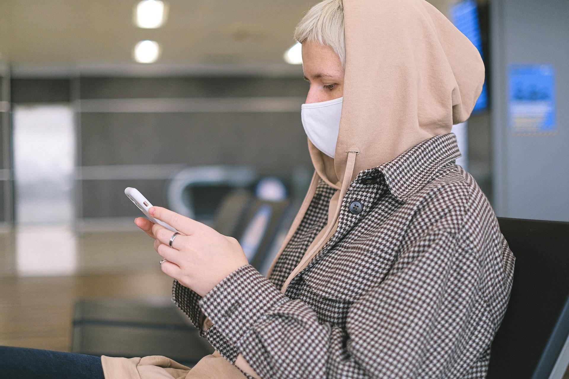 Woman in a face mask using her smartphone, sitting in an airport waiting area.