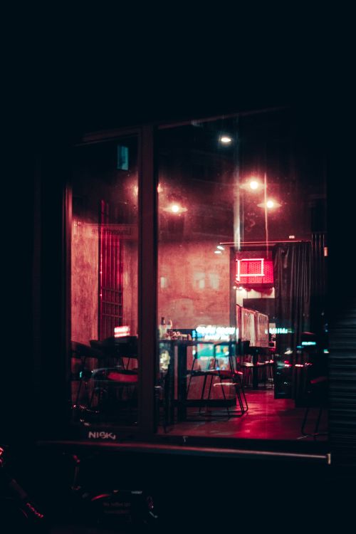 Free A dimly lit urban cafe visible through a glass window, captured at night. Stock Photo