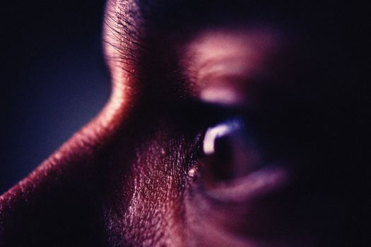 Artistic close-up image capturing the intense detail of an eye under dark lighting conditions.
