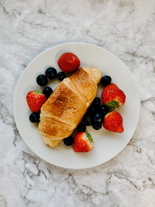 Free Top view of delicious breakfast with fresh strawberries and blueberries with crusty croissant on white plate Stock Photo