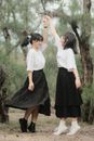 Full body of positive ethnic female holding hand of friend and spinning around in nature with evergreen trees