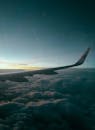 Wing of airplane flying over clouds at sundown