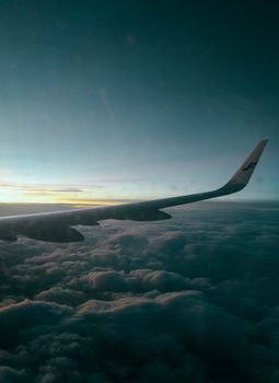 Amazing scenery of wing of airplane flying over fluffy clouds in sunset sky