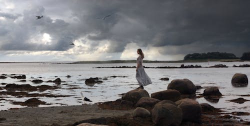 Woman Standing on a Rock Near Sea  Under A Gloomy Sky