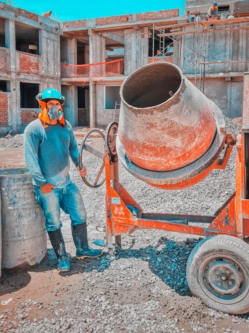 Construction Worker Standing Beside A Concrete Mixer