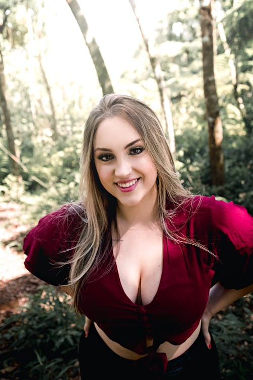 Positive young woman standing in forest with hands on waist and smiling