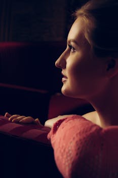 An elegant side profile of a young woman in low lighting, evoking contemplation and grace.