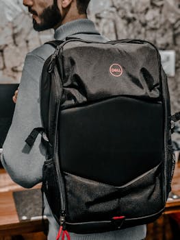 Close-up of a man wearing a Dell backpack indoors with a blurred background.