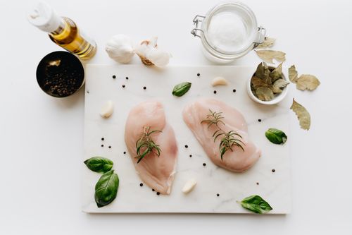 Free Top view of raw chicken breasts with herbs and spices on a marble board, ready for cooking. Stock Photo