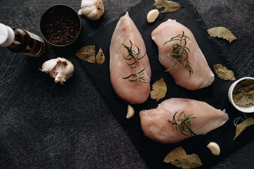 Free Top view of raw chicken breasts with fresh herbs, garlic, and bay leaves on a dark surface, ready for cooking. Stock Photo