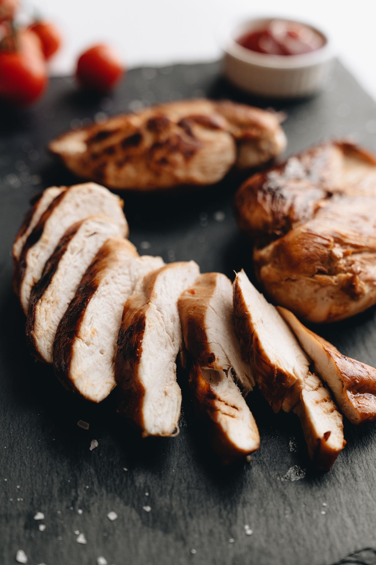 Sliced grilled chicken breasts on slate with tomato garnish
