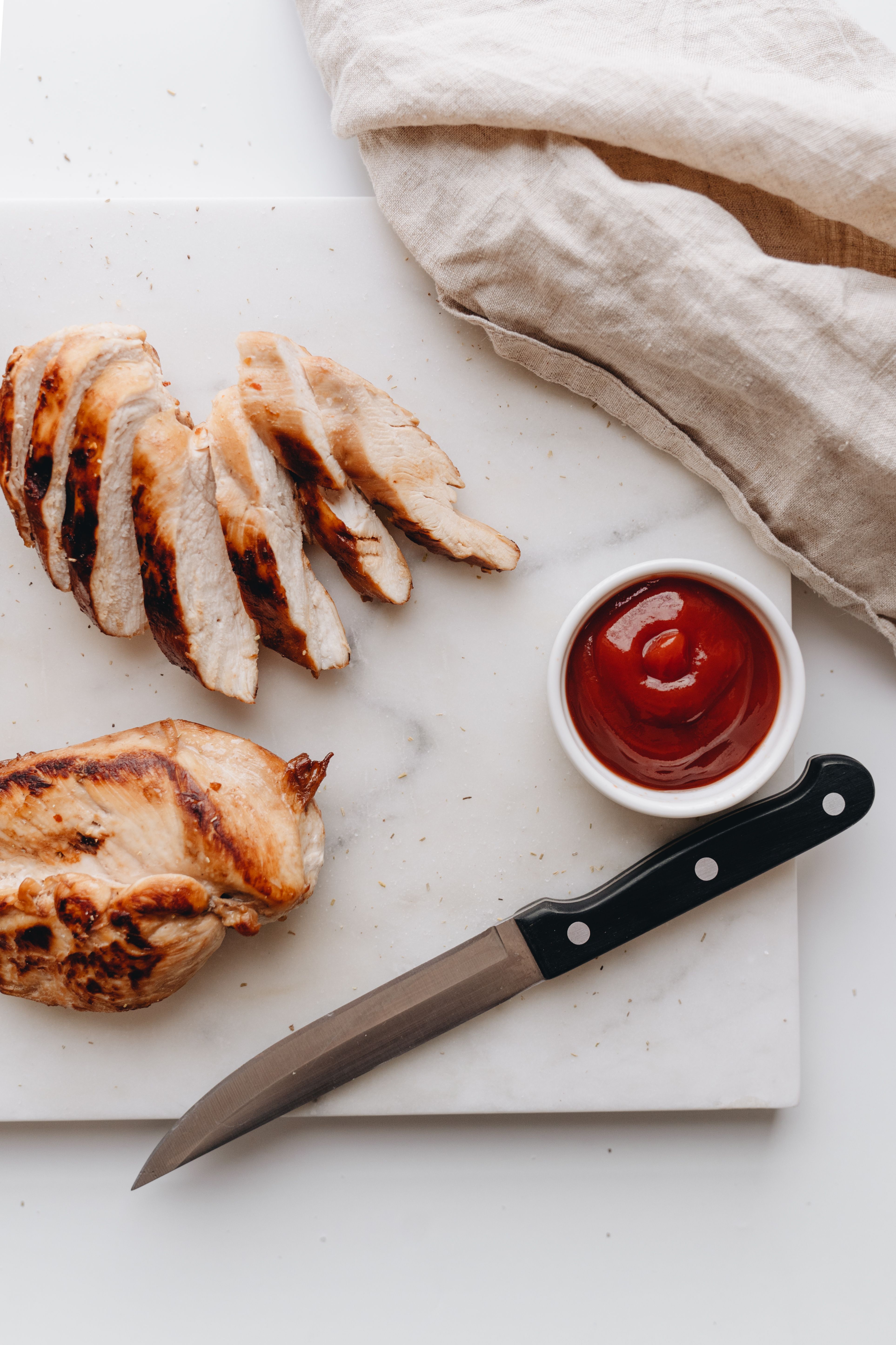 Top view of grilled chicken breast slices with ketchup on a marble board.