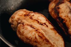 Two beautifully cooked chicken breasts searing on a non-stick frying pan.