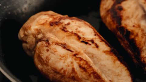 Two beautifully cooked chicken breasts searing on a non-stick frying pan.