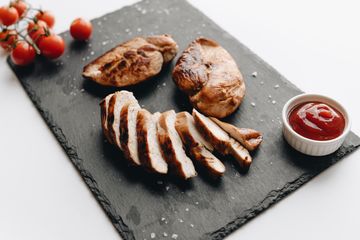 Sliced grilled chicken breast on a slate board with ketchup and cherry tomatoes