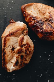 Juicy grilled chicken breasts with a crispy texture on a dark slate.