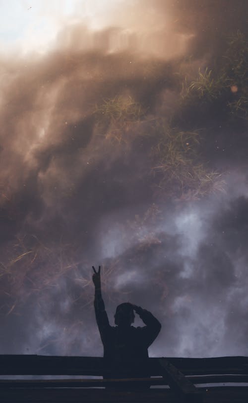 Anonymous person showing victory gesture against sunset clouds