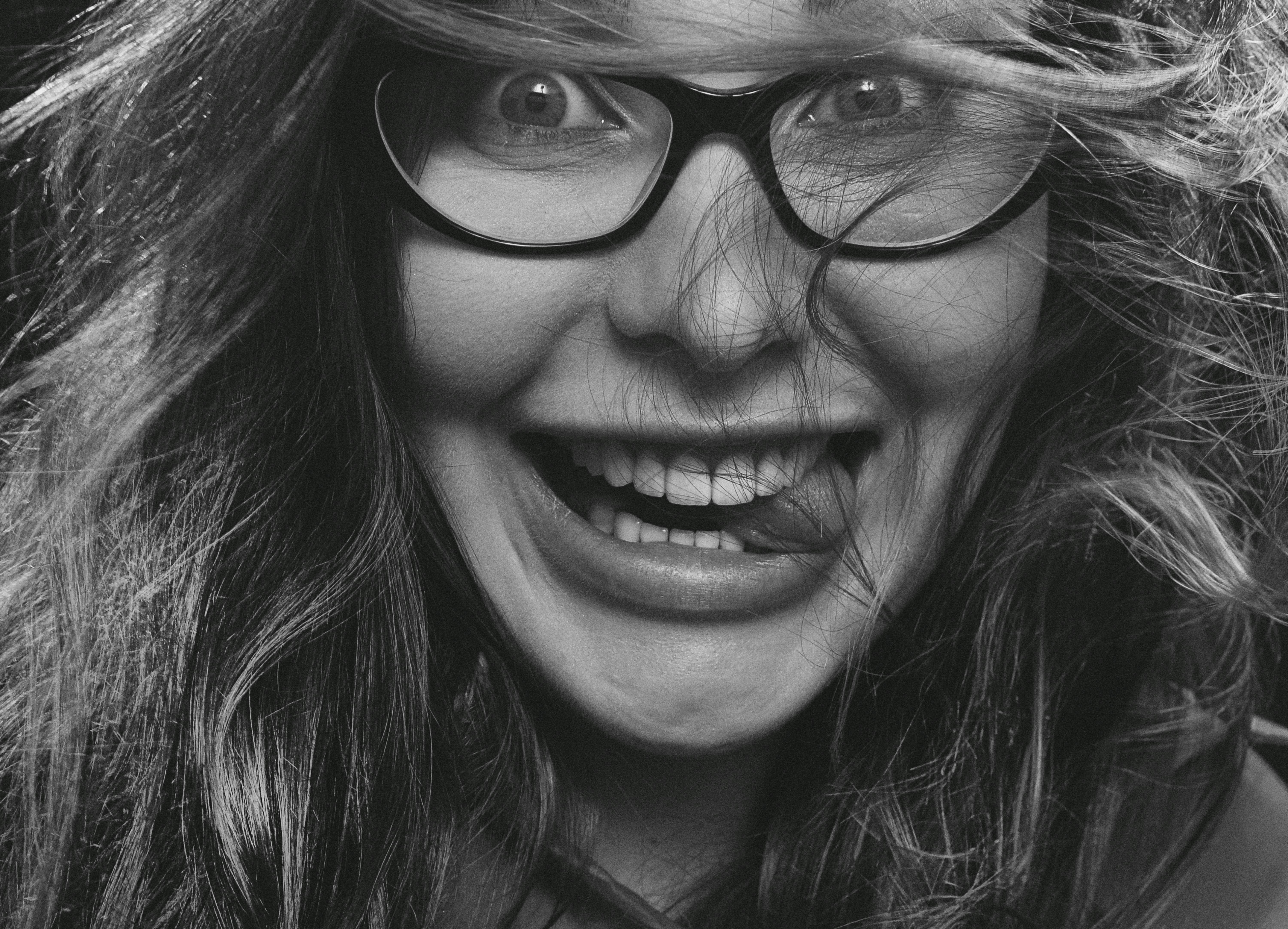 Vibrant close-up of a woman gleefully posing with glasses in grayscale.