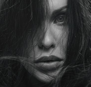 Striking grayscale close-up of a woman's face with hair framing her intense gaze.