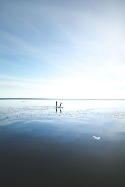 Distant unrecognizable person standing on paddleboard in calm sea water and rowing against cloudy blue sky