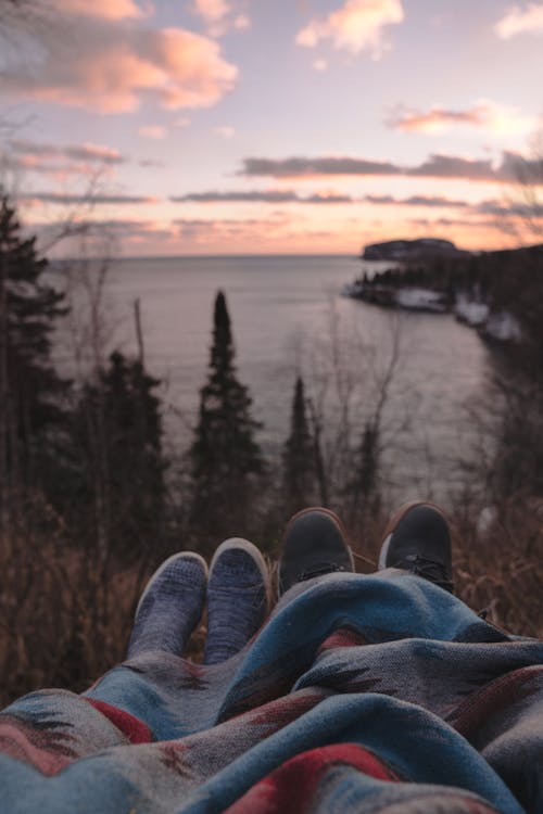 Anonymous couple lying on hill at seaside and enjoying sunset time