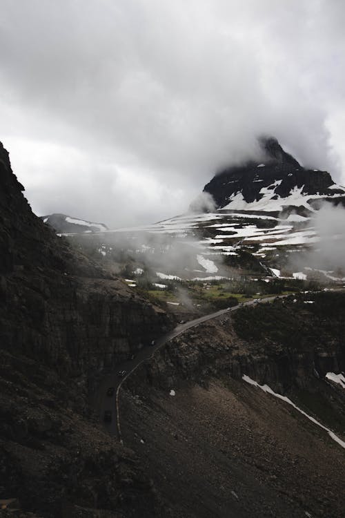 Rough slope of rocky mountain with snowy peaks under thick gray clouds on gloomy day