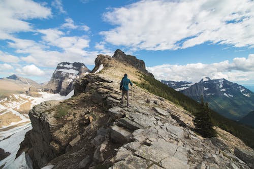 Anonymous male traveler walking on rocky mountain slope in wild valley