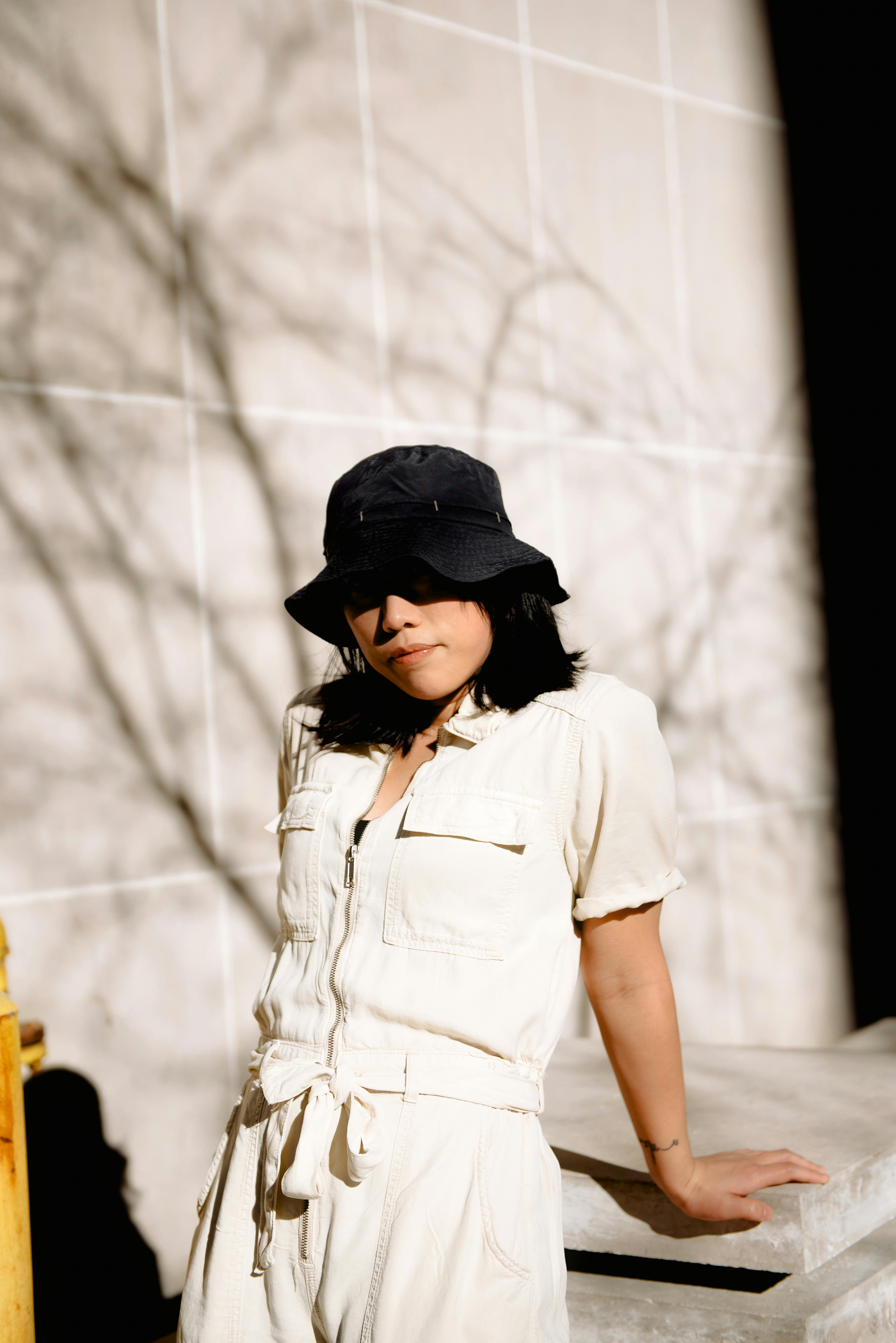 Confident female in casual outfit covering eyes with panama standing near concrete slab in sunshine