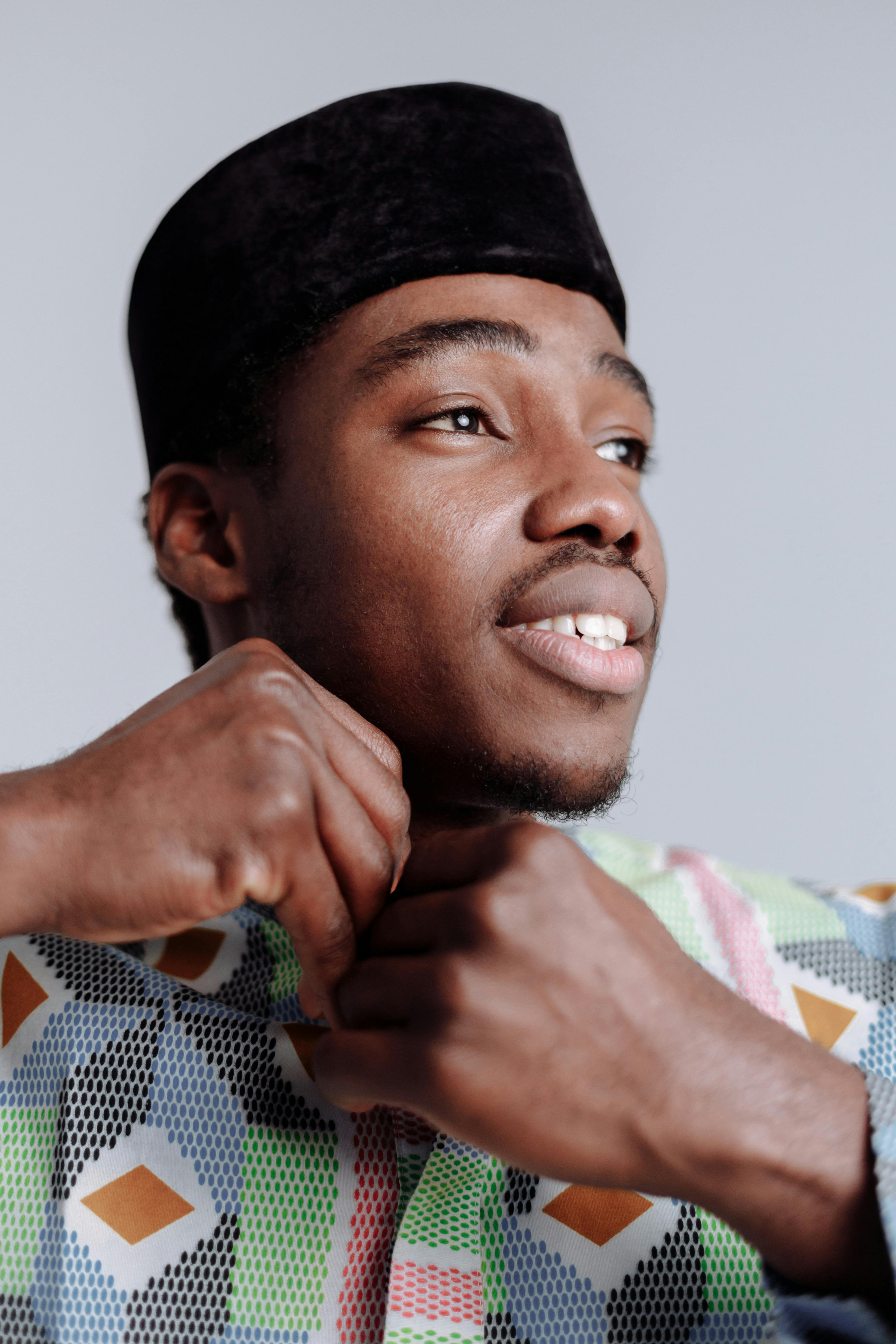 Close-up of a young black man buttoning a multicolored shirt, showcasing fashion and tradition.
