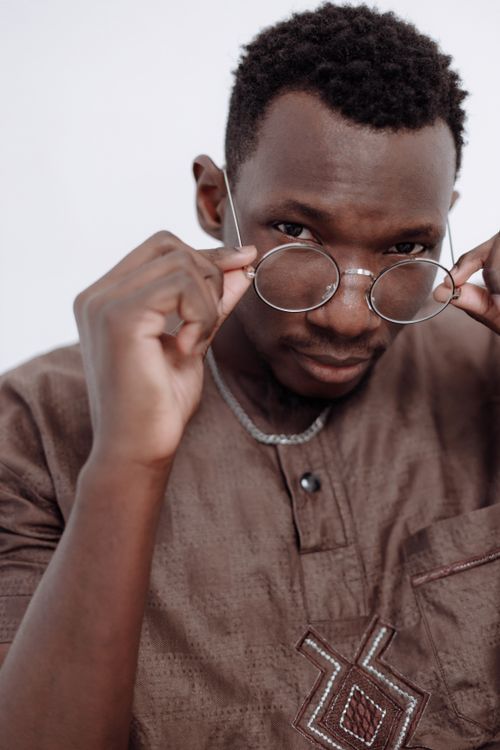 Free Close-up portrait of a young man adjusting his eyeglasses, wearing a brown traditional shirt. Stock Photo