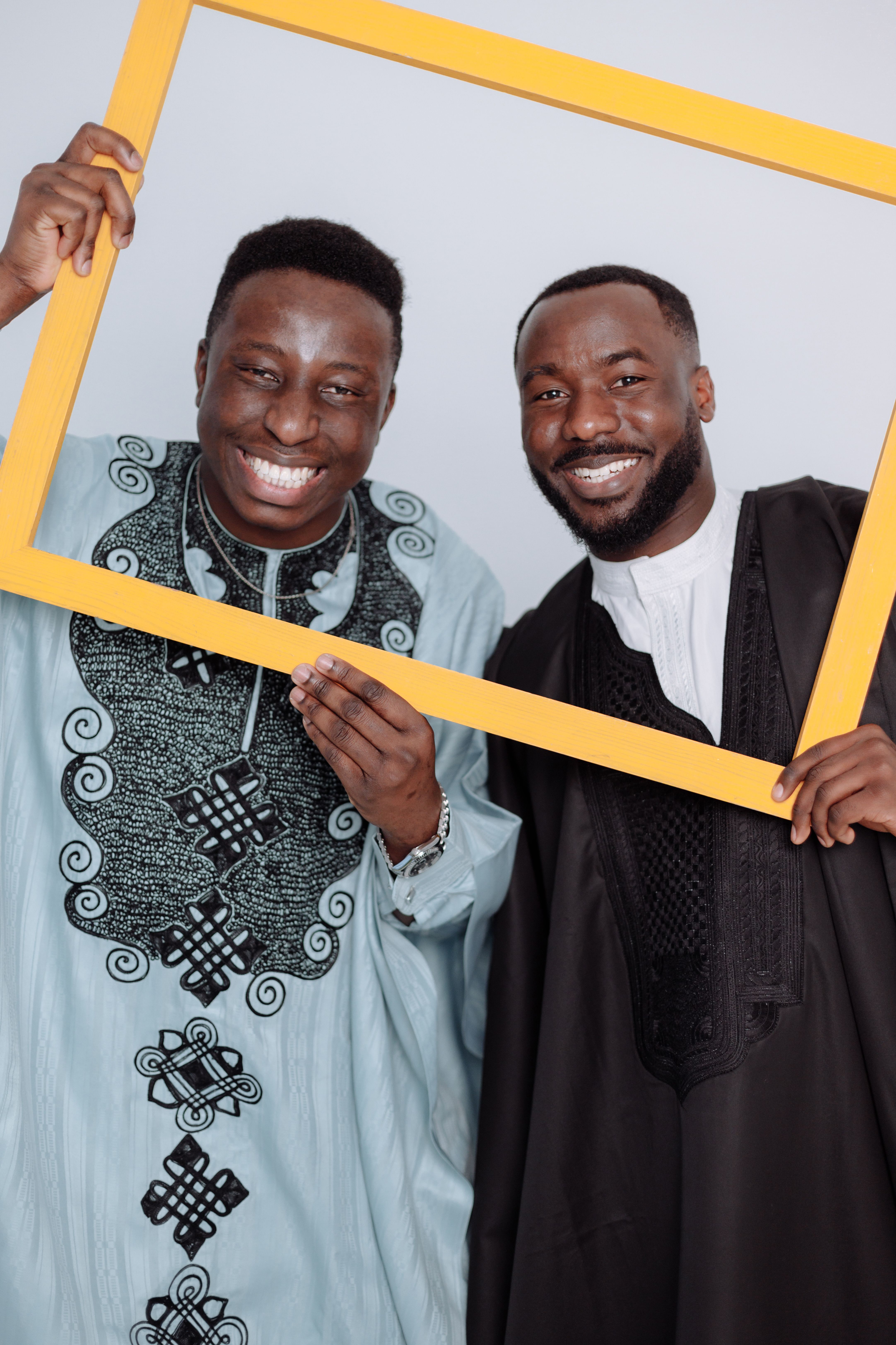 Smiling African men in traditional attire holding a yellow frame in a studio setting.