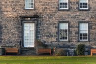 Exterior of old fashioned stone building with windows and door located on grassy lawn with wooden benches in suburb area