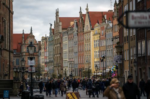 Free Crowd of people in outerwear walking on paved walkway near aged colorful residential houses on street with streetlight in city Stock Photo