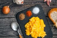 Top view of delicious scrambled eggs served on black board with colorful spices on wooden table with onion and slice of bread