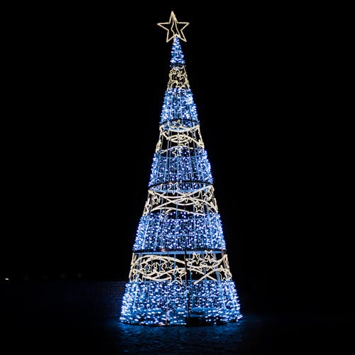 Free Illuminated Christmas tree with glowing golden and blue garlands topped with decorative star placed on black background during holiday celebration Stock Photo