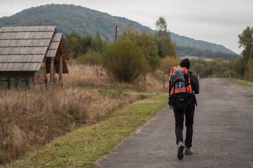 Unrecognizable backpacker walking on road near wooden house