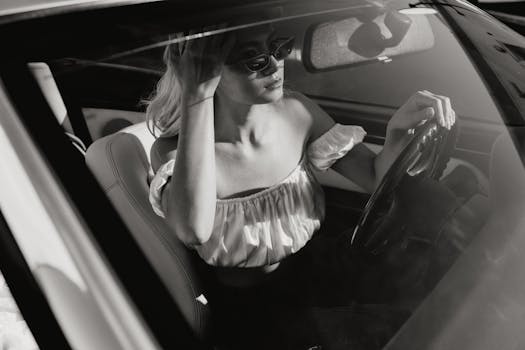 Black and white image of a woman driving a vintage car, showcasing elegance and style.
