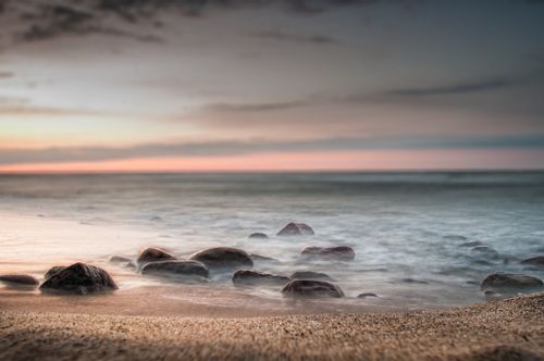 Free Sandy beach with rocks near rippling sea with horizon line against colorful sky at sundown time in nature in tropical country Stock Photo