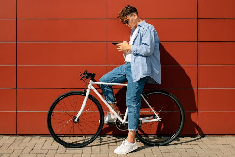 A Man Sitting On A Bicycle While Using His Phone