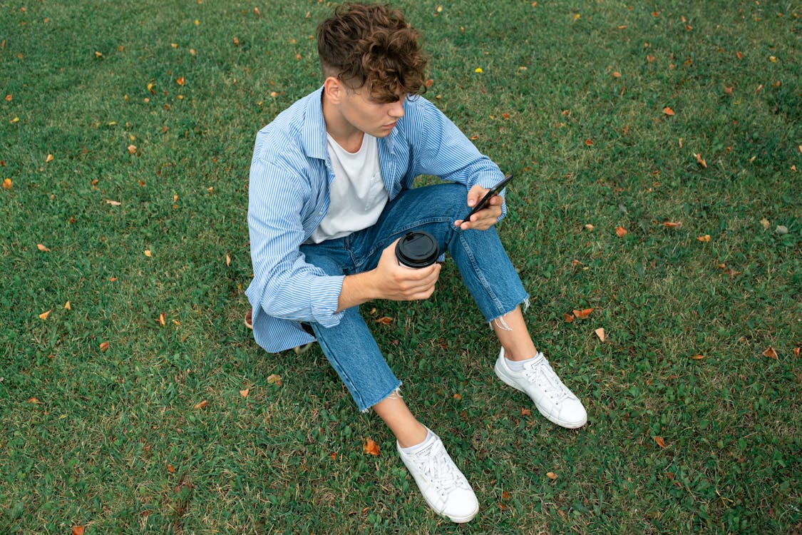 A Man Browsing a Smartphone while Holding a Coffee Cup