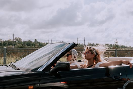 Two fashionable women driving a convertible with sunglasses, capturing the essence of freedom and style.