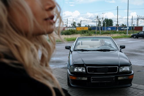 白い車の横に立っている黒いジャケットの女性