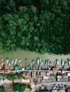 Drone view of typical settlement with residential building and parked cars located on gulf of sea with moored on piers boats and green trees