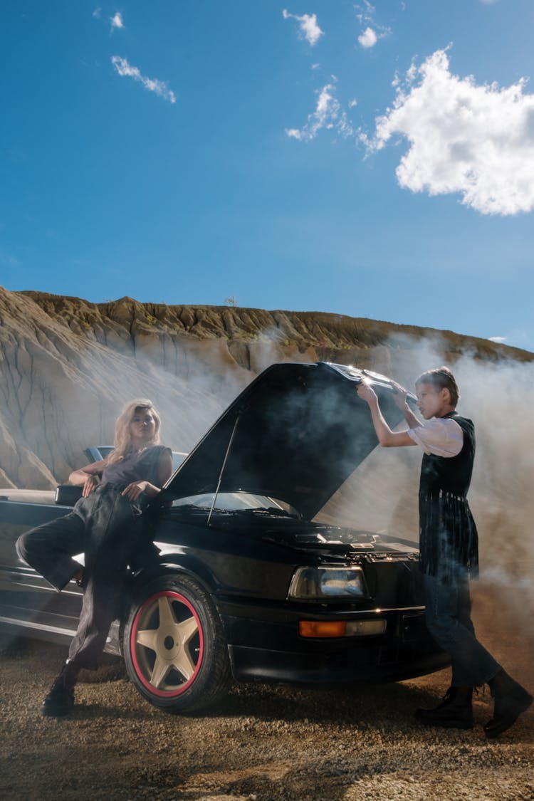 A Man And Woman Standing Near The Smoking Car