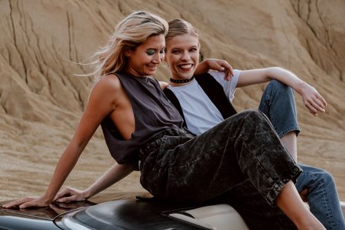 Free Two women sitting on a car, smiling and relaxing in a desert landscape. Stock Photo