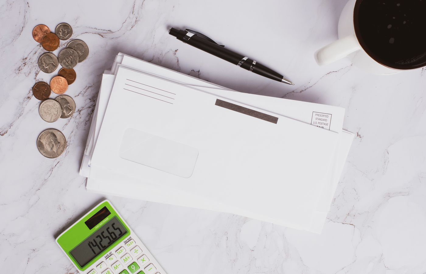 Flat lay of financial documents, calculator, coins, and coffee cup on marble surface.